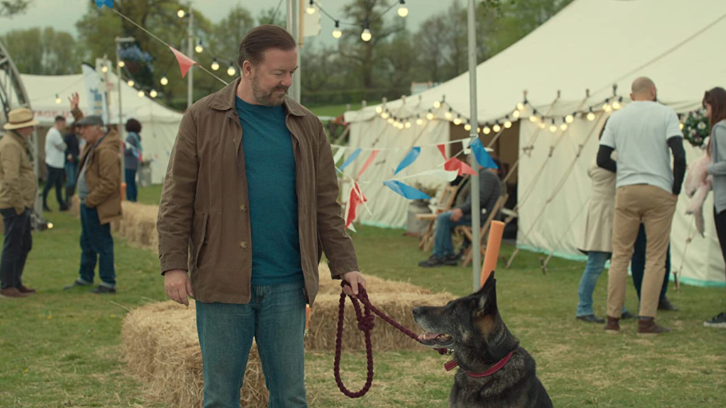 Tony Johnson, played by actor Ricky Gervais stands with his dog, Brandy, at a town fair in the show 'After Life'.